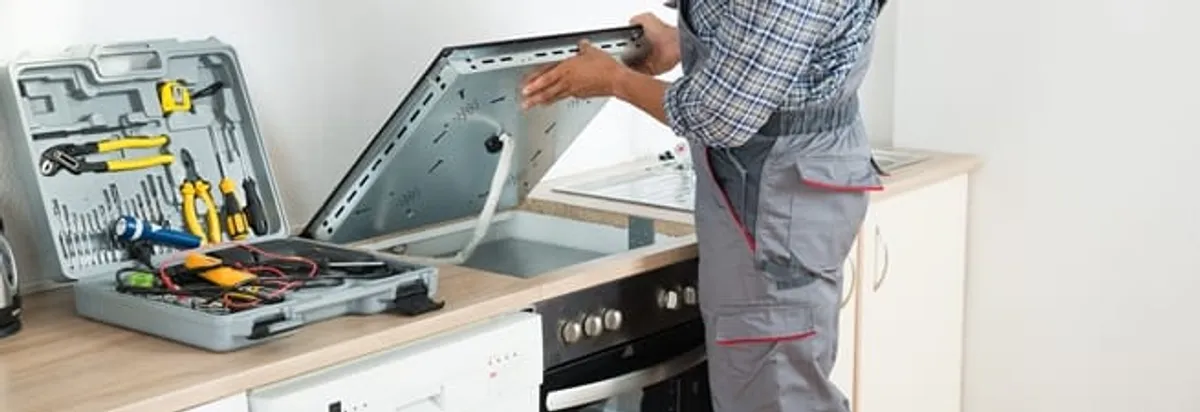 Cooktop repair technician lifting a built-in stovetop for service in El Paso, TX
