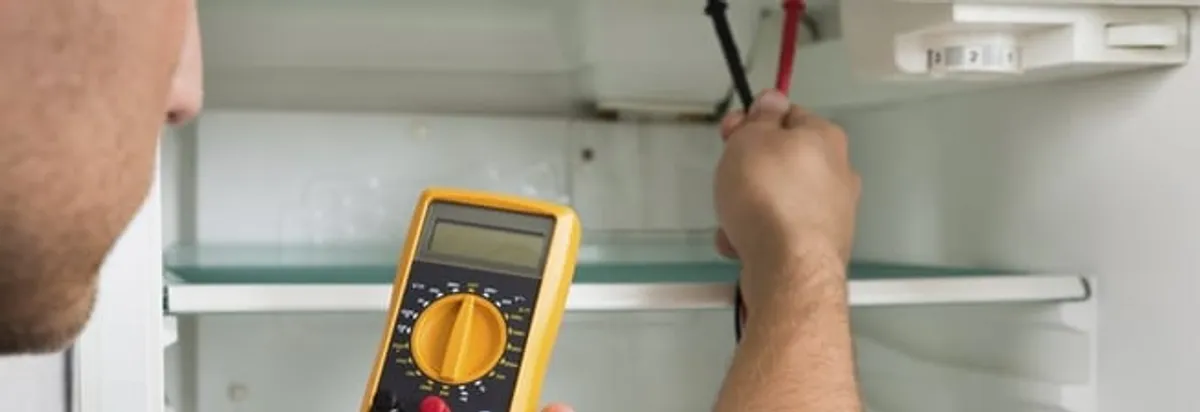 Refrigerator repair technician testing electrical components with a multimeter in El Paso, TX
