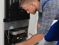 Refrigerator repair technician servicing the compressor and condenser area in El Paso, TX